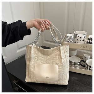 Detail of the woven straw tote bag featuring a leather front pocket and chain shoulder strap