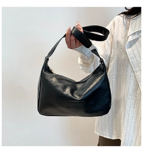 Detail of minimalist black PU leather shoulder bag with wide strap and fashion label