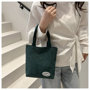 Detail of dark green corduroy handbag with FANYISSA logo held by a model on white stairs
