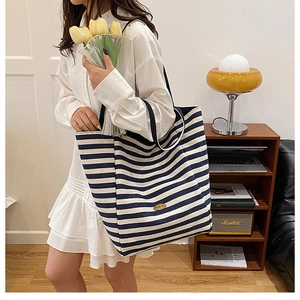 Detail of striped knit tote bag with gold logo plate and nautical navy blue patterns