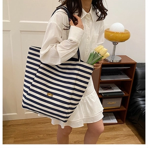 Detail of blue and white striped canvas tote bag with gold metal plaque on model's shoulder