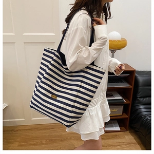 Blue and white striped canvas tote bag shown worn by a model in a cozy home setting