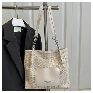 Close-up of woven straw tote bag with leather pocket patch and silver chain strap
