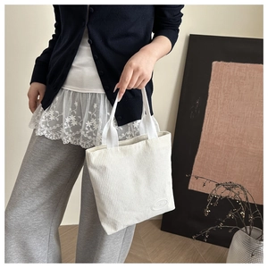Detail shot of beige corduroy tote bag showing ribbed texture and brand logo patch