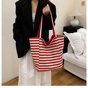 Detail of red and white striped canvas tote bag with gold metal logo on a model