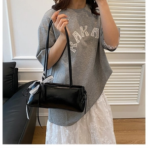 Détail du sac sous l'aisselle noir avec nœud en dentelle blanche, pompons et cuir PU brillant