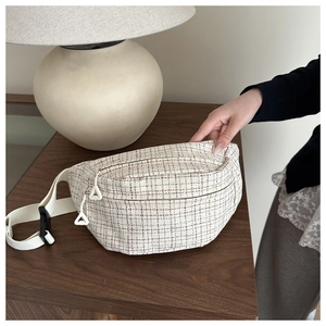 Close-up of cream tweed chest bag featuring dual zippers on a rustic wooden table