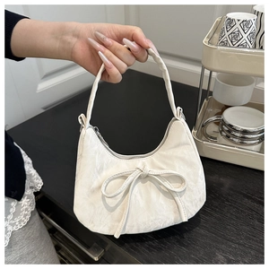 Detail einer cremeweißen Hobo-Tasche mit großer Schleifendekoration und Texturmaterial