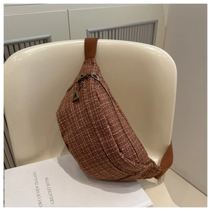 Detail of brown tweed waist bag featuring dual zippers on a beige chair with a book