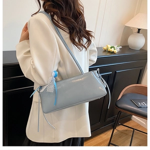 Détail du sac à bandoulière en cuir verni bleu clair avec accessoire nœud en dentelle