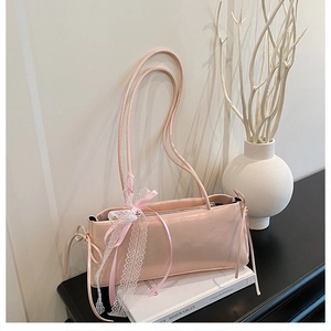 Détail du sac baguette rose avec dentelle blanche et nœud sur une surface noire