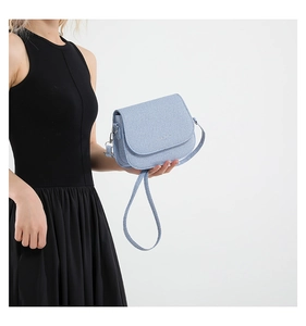 Détail d'un sac selle en tissu texturé bleu clair avec rabat et bandoulière fine