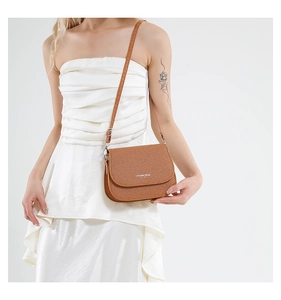 Détail d'un sac besace marron texturé avec boucle argentée porté sur une robe blanche