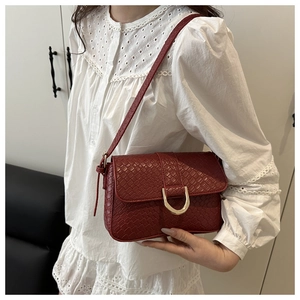 Detail van bordeauxrode geweven crossbodytas met gouden hoefijzervormige metalen gesp en riem