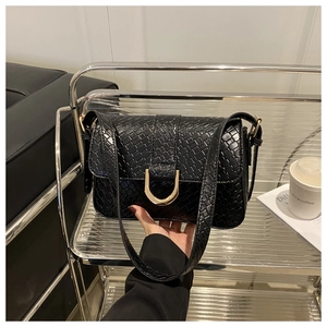 Detail van zwarte crossbody tas met krokodillenpatroon en gouden hoefijzersluiting