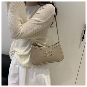 Side view of beige crescent underarm bag with golden bow buckle on model