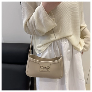 Close-up of beige minimalist shoulder bag with gold bow detail and smooth leather finish