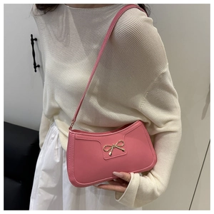 Detail of pink shoulder bag with gold metal bow on a knit sweater background