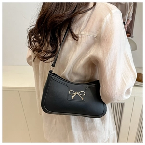 Close-up of a black minimalist underarm bag with a decorative gold metal bow buckle