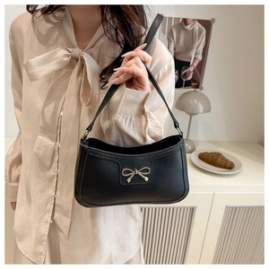 Close-up of black leather crescent armpit bag with gold bow detail on female model