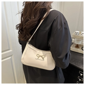 Detail of cream shoulder bag with golden bow buckle and smooth leather texture