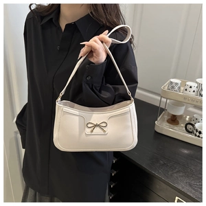 Detail of white half-moon underarm bag featuring a delicate golden metal bow accent