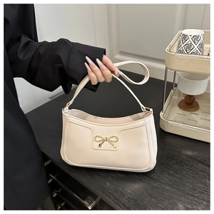 Detail of a creamy white crescent bag featuring a golden bow buckle and smooth leather texture