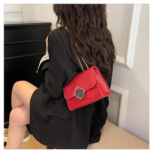 Detail of red woven texture shoulder bag with gold chain strap on a black blazer