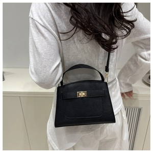 Gros plan sur le cuir grainé noir et le fermoir rotatif doré de ce sac à main chic