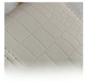 Close-up of beige crocodile embossed leather and precise stitching detail on shoulder bag
