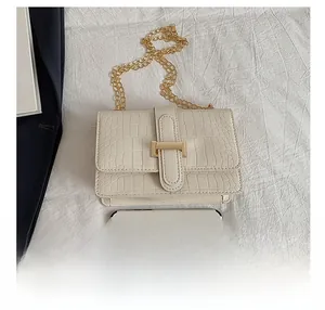 Detail showing white crocodile texture crossbody bag with gold H-buckle and chain strap