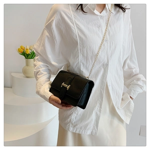 Detail of a black textured leather crossbody bag with elegant gold chain and metal buckle