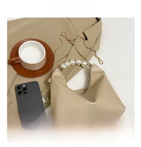 Detail of beige hobo bag with pearl handle and golden chain next to a smartphone