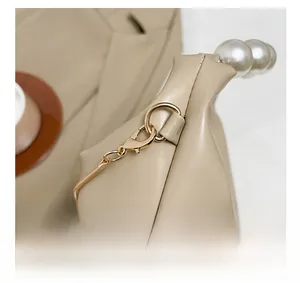 Close-up of golden hardware connectors and elegant white pearls on a beige chain bag