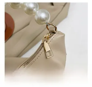 Detail of smooth metal zipper and elegant large pearl handle on beige dumpling bag