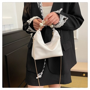Detail of white semi-circular shoulder bag with large pearl handle and gold chain strap
