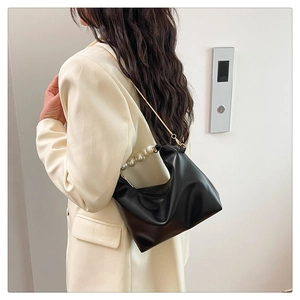 Black leather pillow bag featuring large pearl handle and gold chain on a model