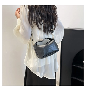 Detail of black geometric patchwork crossbody bag with gold buckle on model shoulder