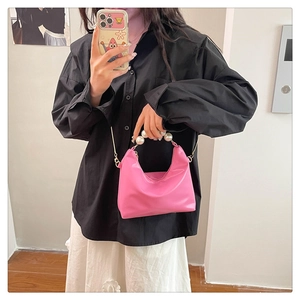 Detail of a bright pink crescent bag with pearl handle and golden chain strap