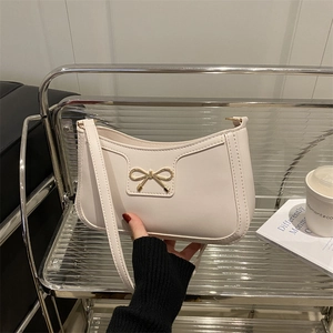 Minimalist cream crescent shoulder bag with a gold bow hardware on a modern metal shelf