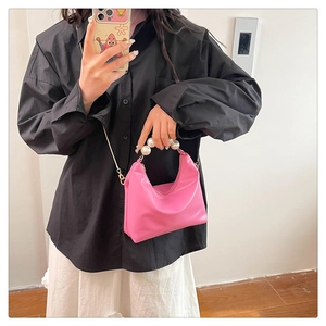 Detail of bright pink mini bag featuring large pearl handle and gold chain strap