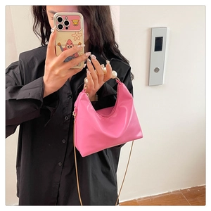 Pink glossy hobo bag with large pearl handle and gold chain strap shown on person