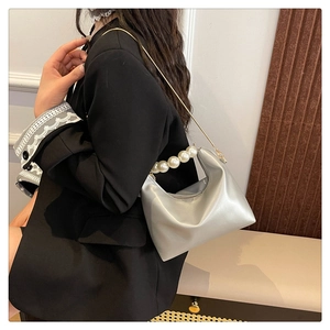 Detail of silver half-moon bag with pearl handle and gold chain on black blazer