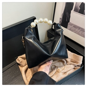 Detail of elegant black dumpling bag featuring a large pearl handle and gold chain strap