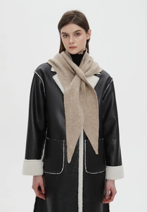 Detail shot of a soft beige knitted long scarf paired with a black faux leather fur coat