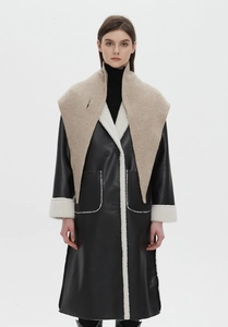 Detail of oversized beige knit shawl collar on a black leather coat with faux fur trim