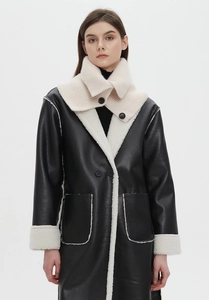 Detail of a beige chunky knit collar layered over a black shearling-lined winter coat