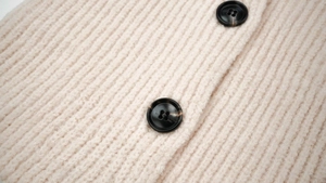 Detailed close-up of light pink ribbed knit fabric with dark tortoiseshell buttons