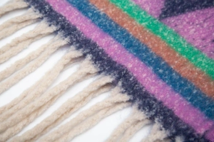 Close-up of thick bouclé knit texture with colorful jacquard patterns and cream tassels