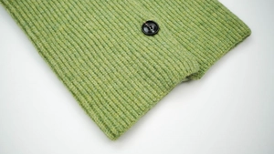 Close-up of green ribbed knit scarf fabric with a black button detail and wool texture